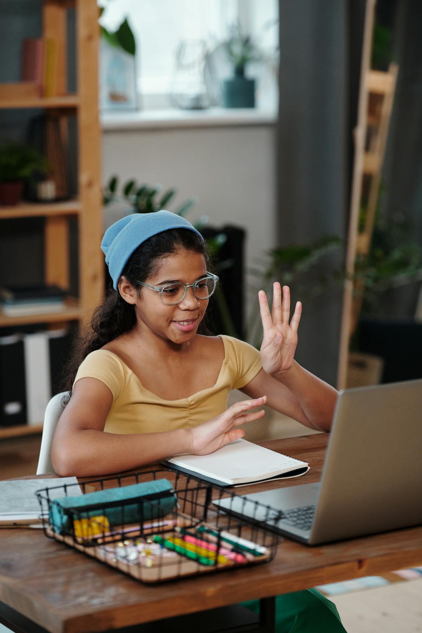 A girl with glasses and a headband participating in an online class from her home.